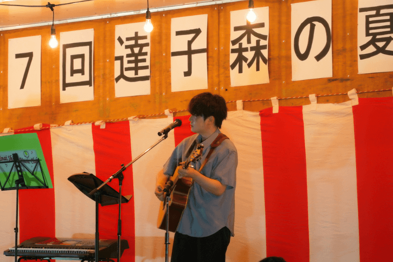 「第17回 達子森の夏祭り」のステージで歌っている音楽クリエイター日景健貴の写真